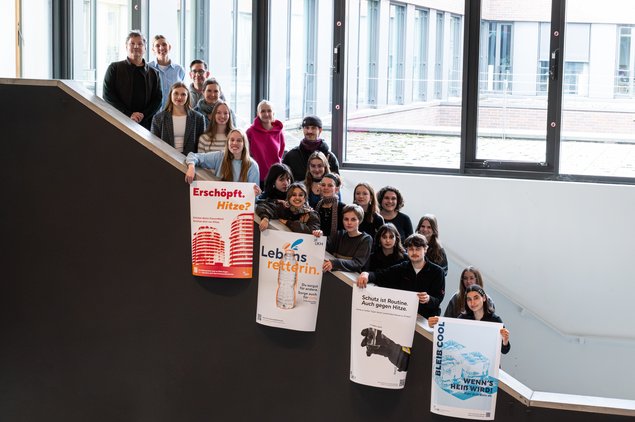 20 Menschen stehen auf einer Treppe und schauen in die Kamera. Einige halten ihre Plakate in der Hand.