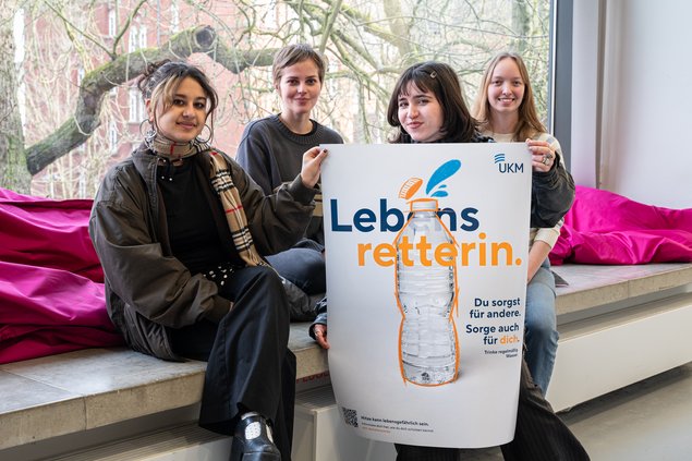 Die Projektgruppe "grid" bestehend aus vier Frauen. Sie sitzen auf einer Fensterbank und halten ihr Plakat mit dem Slogan "Lebensrettern" hoch. Alle lächeln in die Kamera.